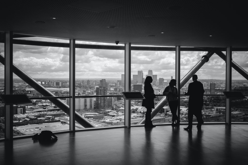 Black and white image of three people looking out window at city skyline | OpenAsset