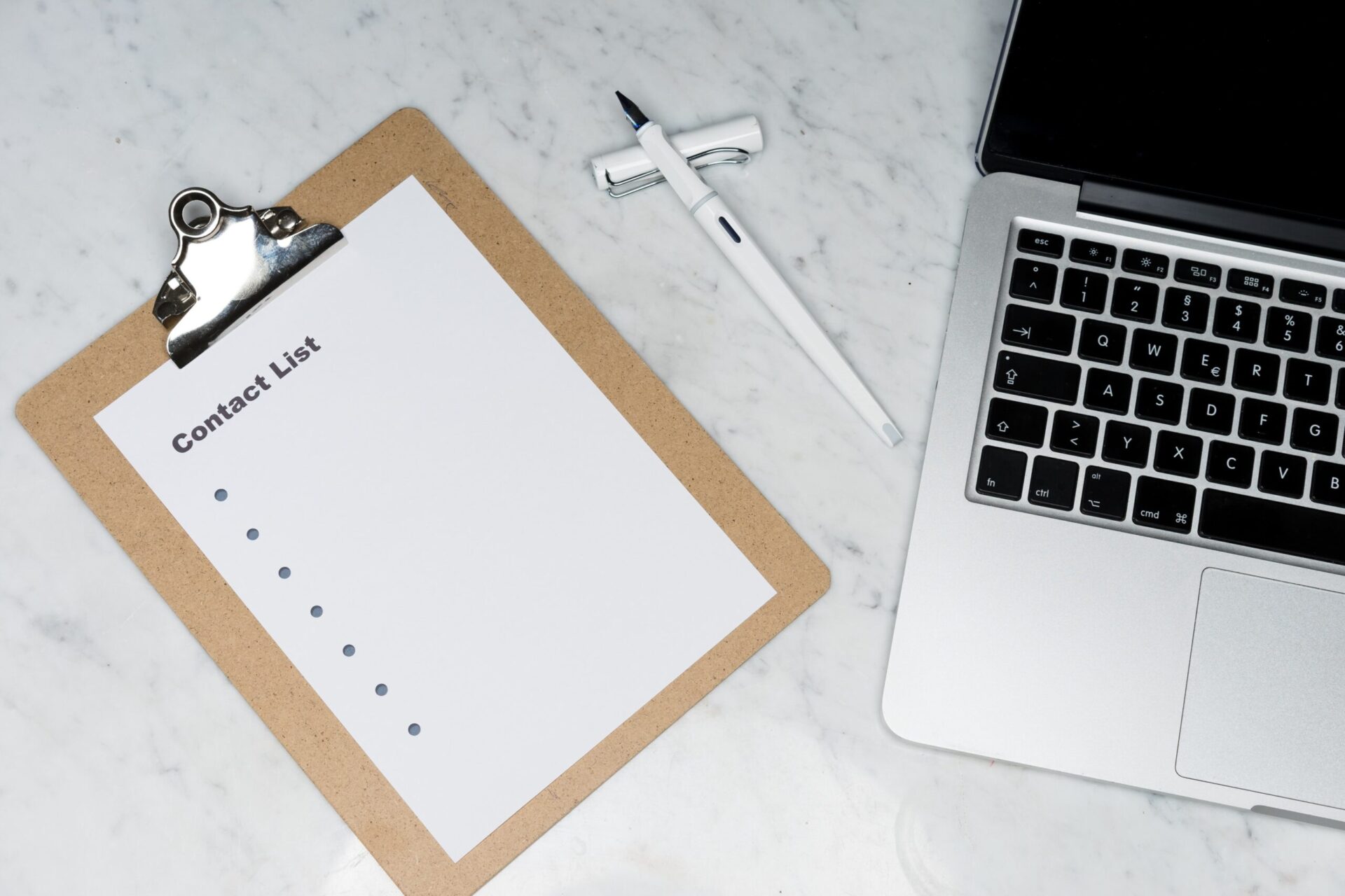 contact list on clipboard on marble surface next to a pen with cap and a laptop | OpenAsset