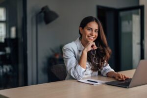 Woman at desk with glasses in hand writing a persuasive proposal